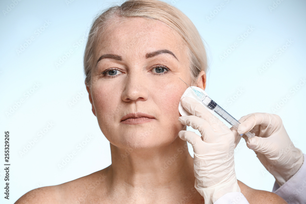 Mature woman receiving injection in face on color background