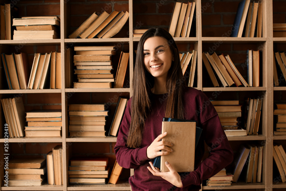 Portrait of beautiful young woman with book in library