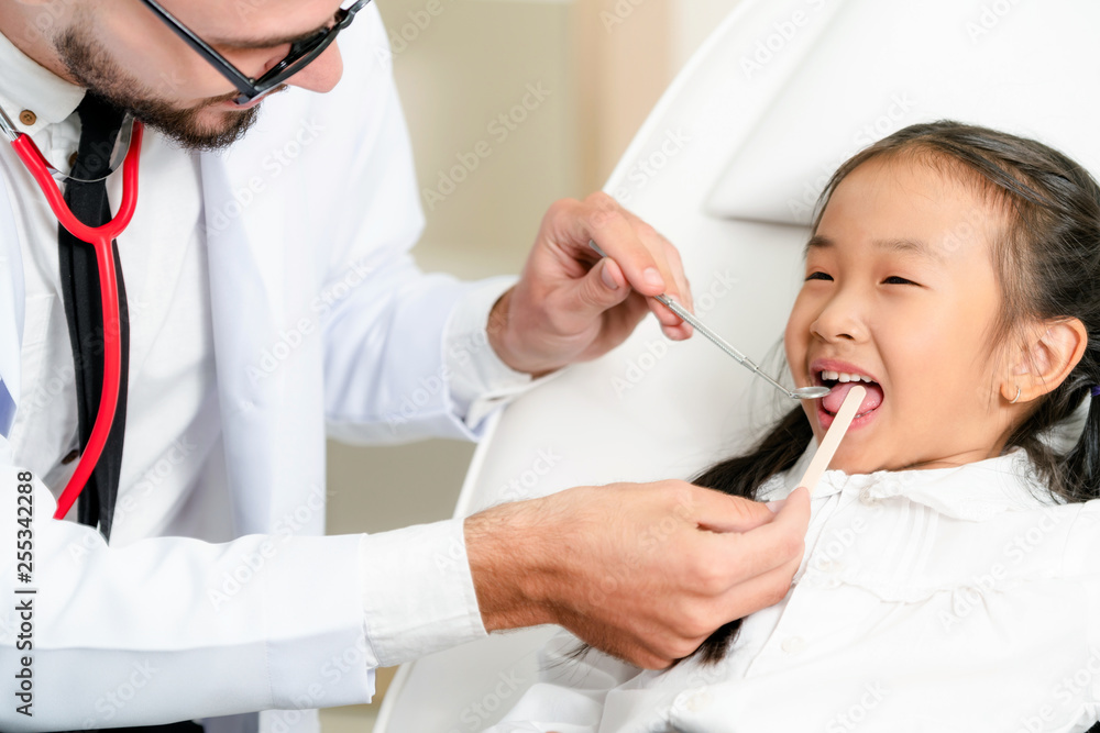 Friendly young dentist examining happy child teeth in dental clinic. Dentistry concept.