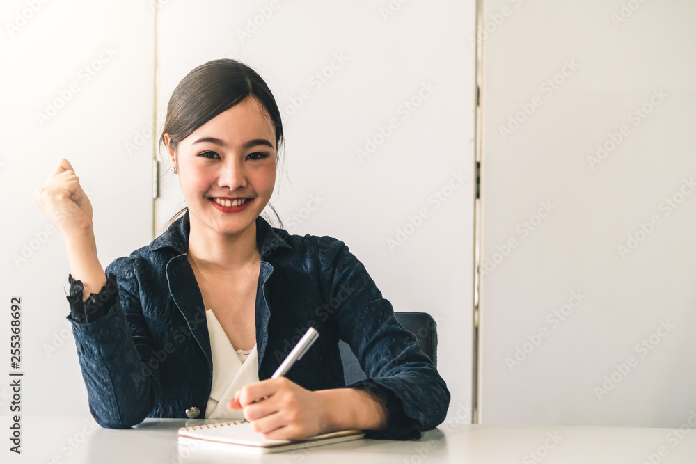 一位年轻漂亮的亚洲美女坐在办公桌旁在笔记本上写信。内容作家a