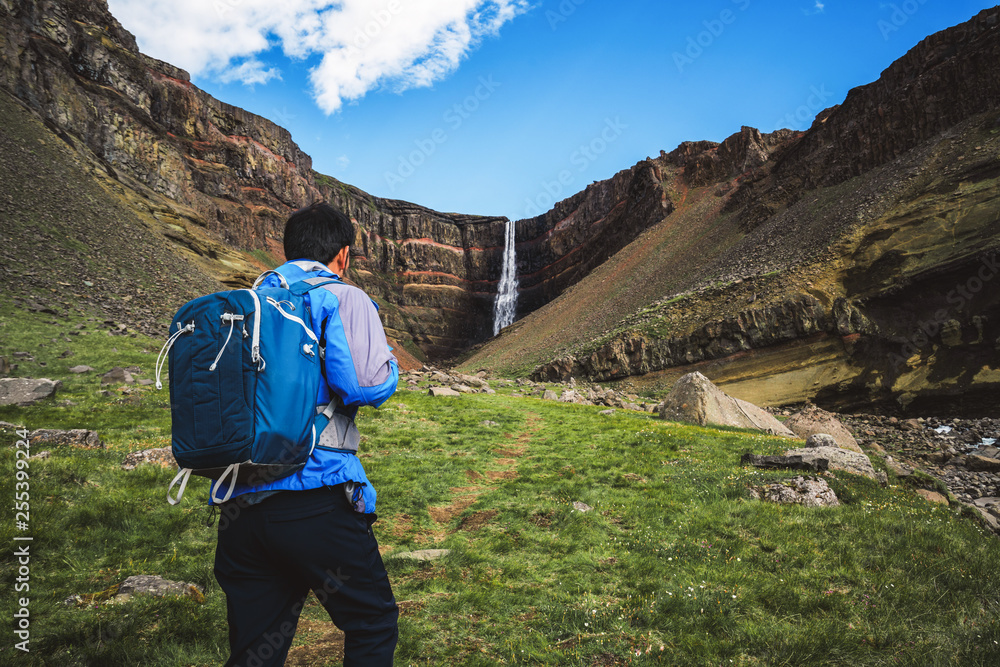 Man traveler hiking in Icelandic summer landscape at the Hengifoss waterfall in Iceland. The waterfa