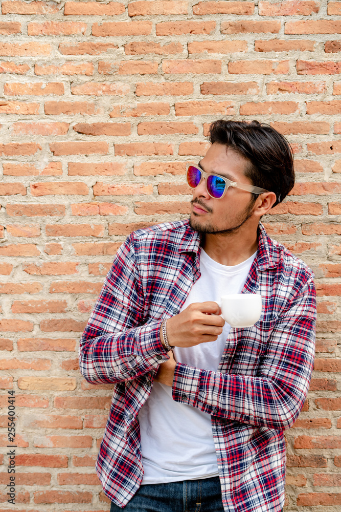 Handsome young man holding coffee cup standing against brick wall.