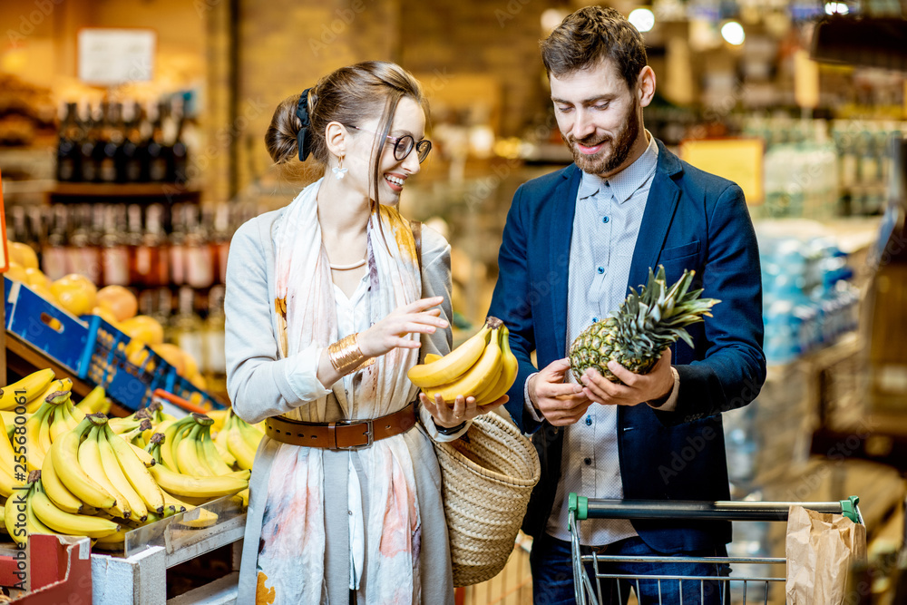 Young and happy couple buying food, choosing fresh fruits in the supermarket