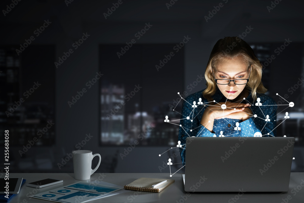 Attractive blonde wearing glasses in dark office using laptop. Mixed media