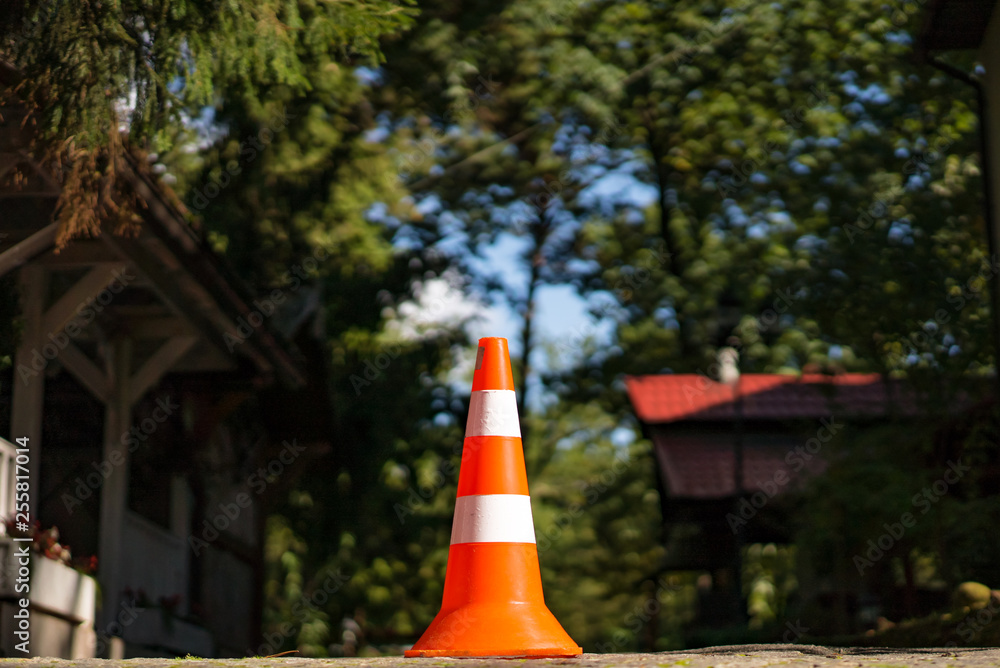 Street cone of two colors with orange and white standing over the natural background. Warning stripe