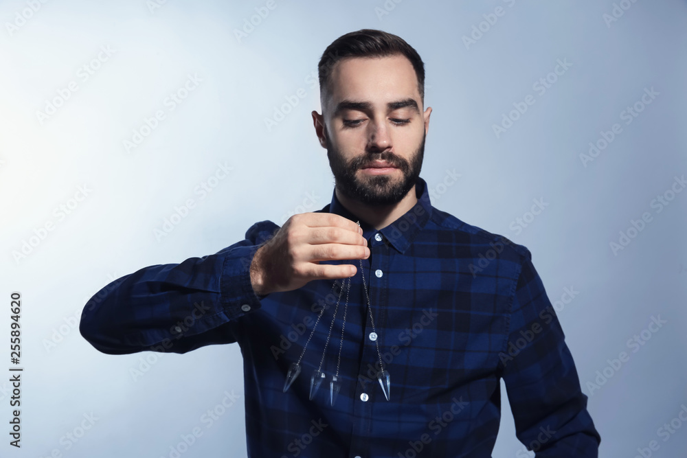 Male hypnotist with swinging pendulum on grey background