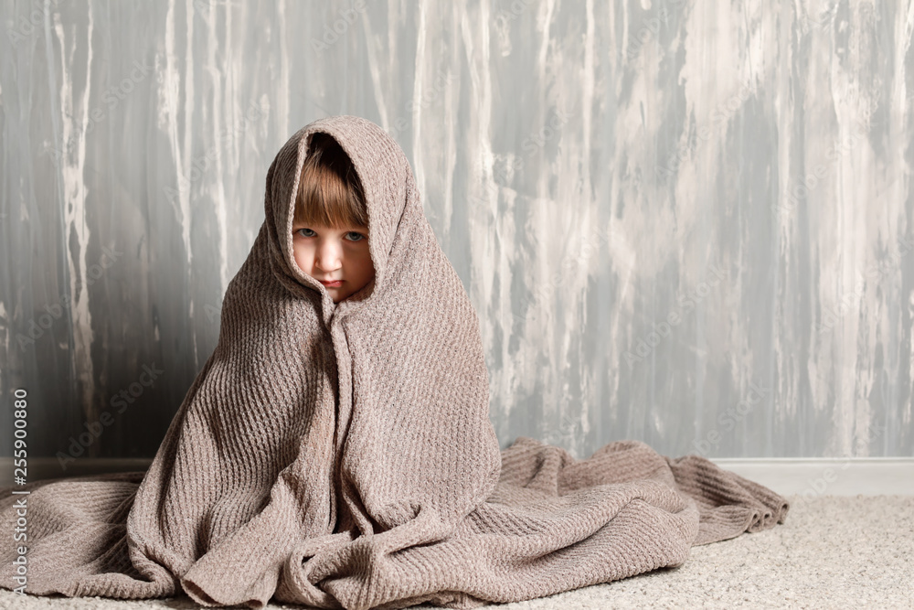 Portrait of sad little girl wrapped in plaid near grey wall