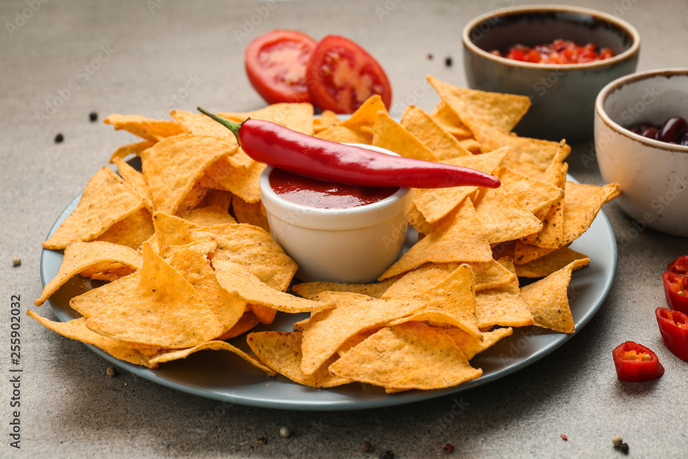 Plate with tasty nachos and tomato sauce on table