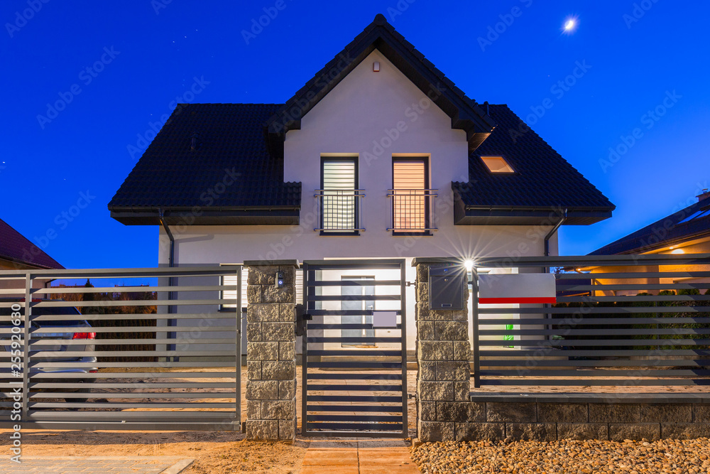 New house with stone fence illuminated at night, Poland