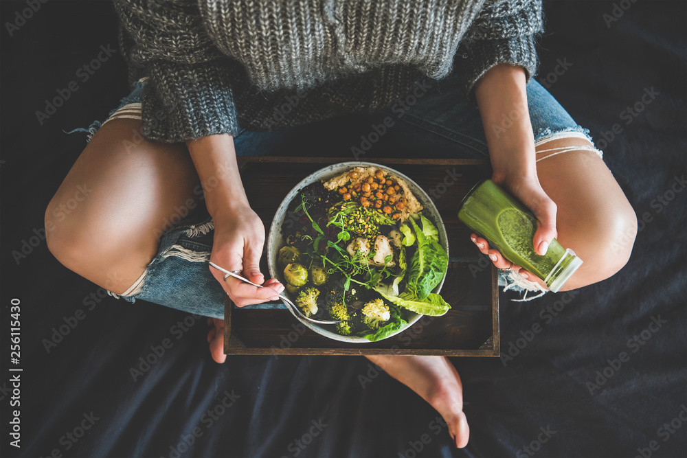 健康的晚餐，床上的午餐。女人坐在床上，吃纯素食超级猫头鹰或鹰嘴豆泥佛碗