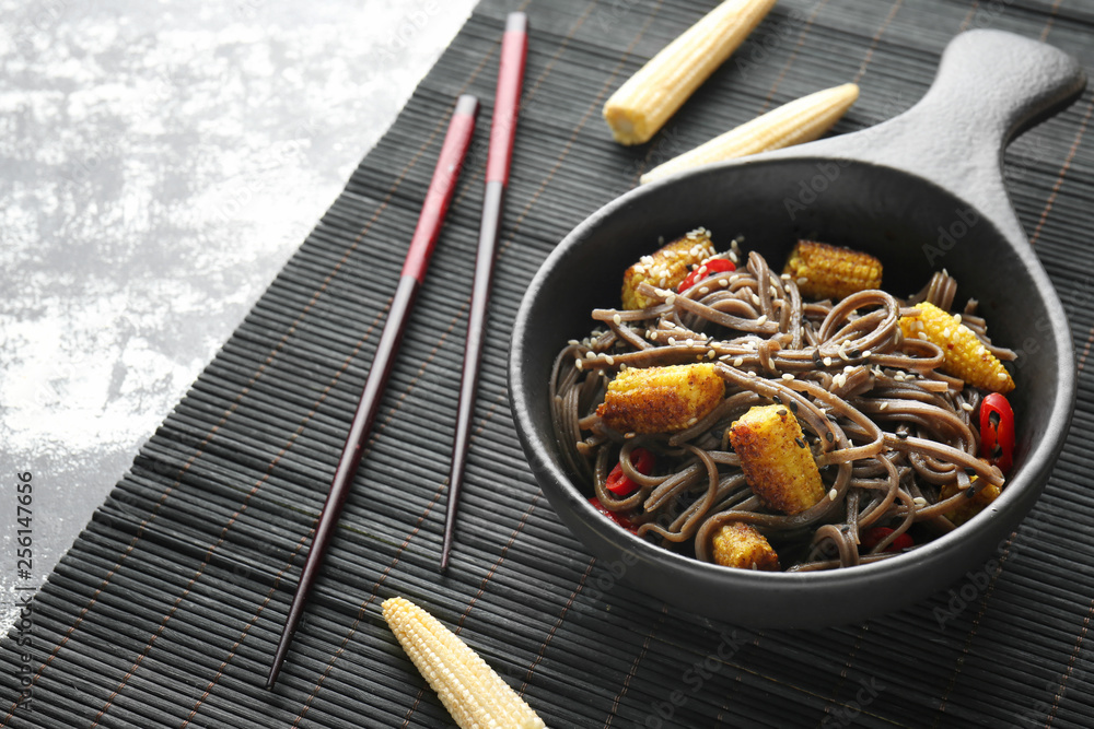 Bowl with tasty soba noodles, corn cobs and chili on table