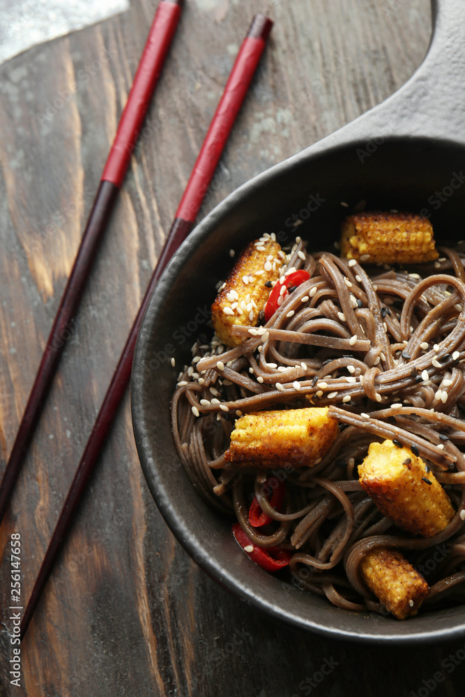 Bowl with tasty soba noodles, corn cobs and chili on wooden board, closeup