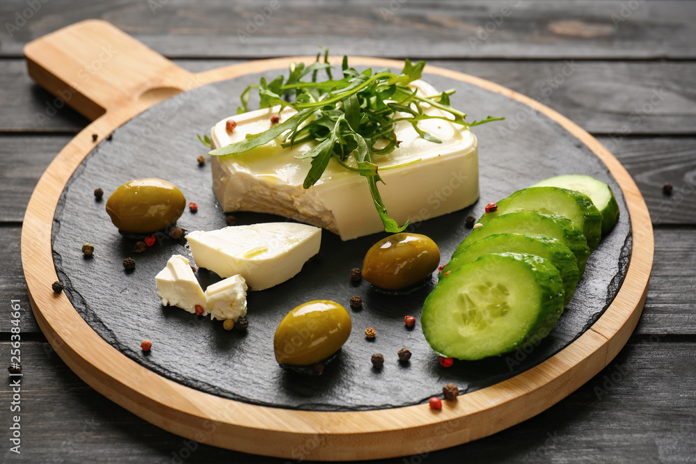 Board with tasty feta cheese, arugula, olives and cucumber on wooden table