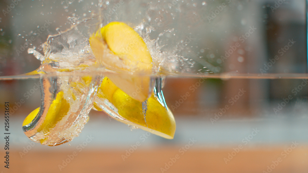 MACRO, DOF: Sweet sliced golden delicious apple falls into the glassy water.