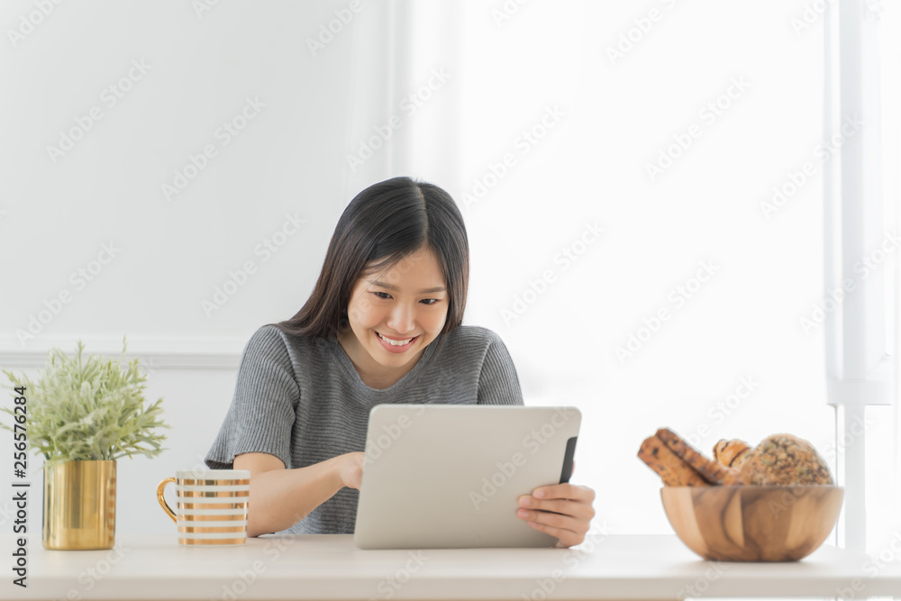 Young Asian woman using tablet at home and having breakfast in the morning .She reading on tablet