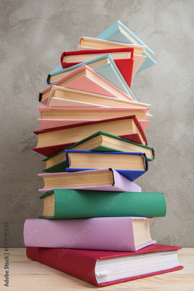 Education and reading concept - group of colorful books on the wooden table, concrete wall blackboar