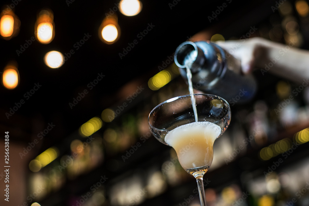 Bartenders hand pouring cocktail into cocktail glass