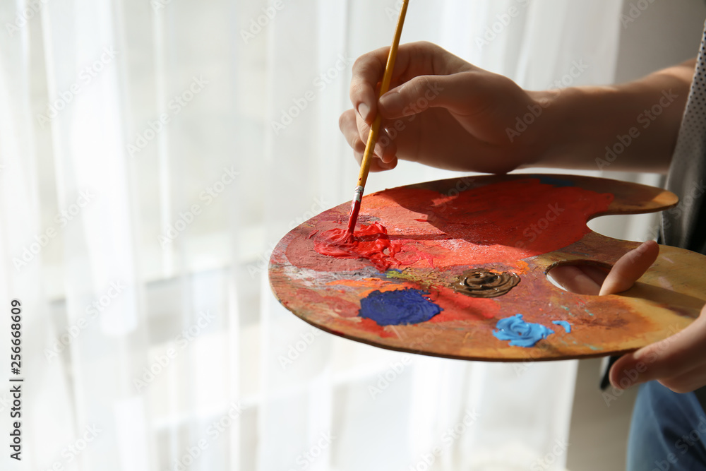 Female artist with paint palette and brush in studio, closeup