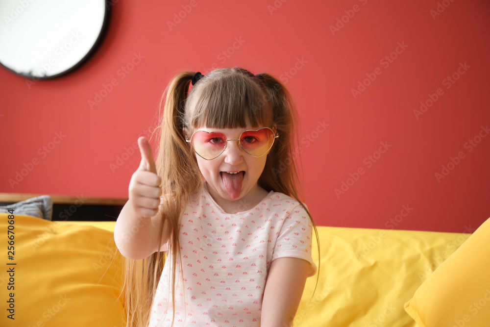 Funny little girl showing thumb-up gesture at home