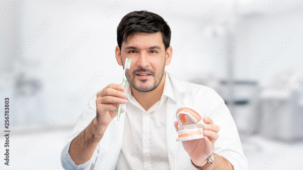 Young male dentist showing toothbrush and denture in dental clinic. Selective focus at the toothbrus