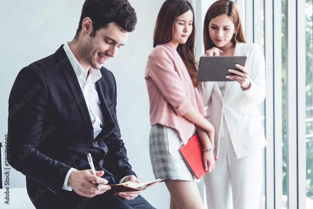 Happy young handsome businessman reading book and working in office with colleagues and friend at wo