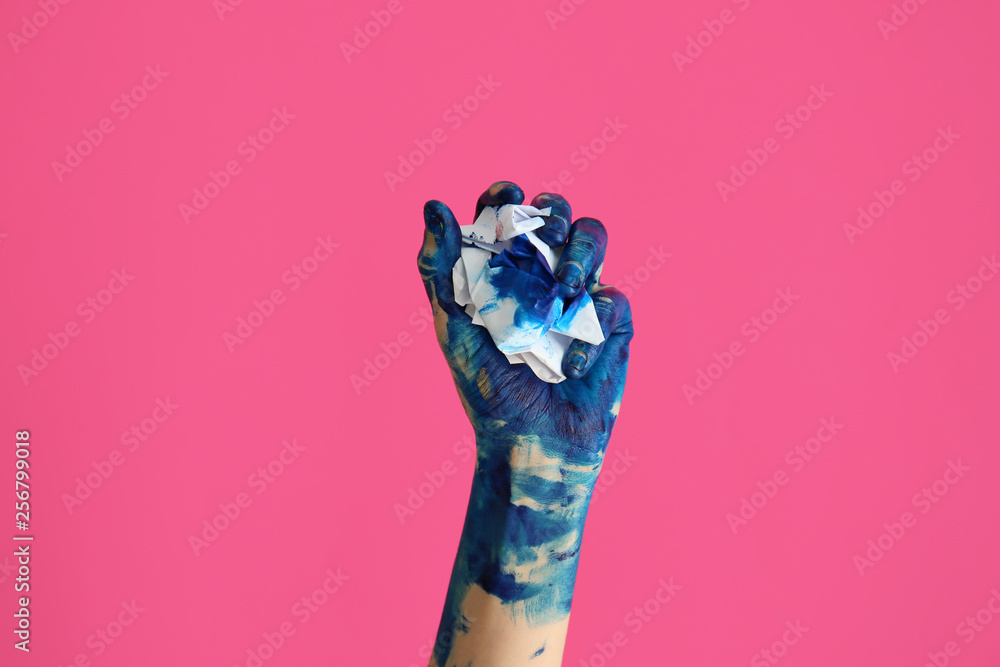 Painted female hand with crumpled paper on color background