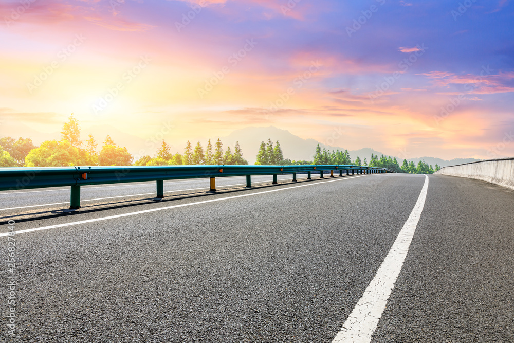 Asphalt highway and forest with mountain scenery at sunset