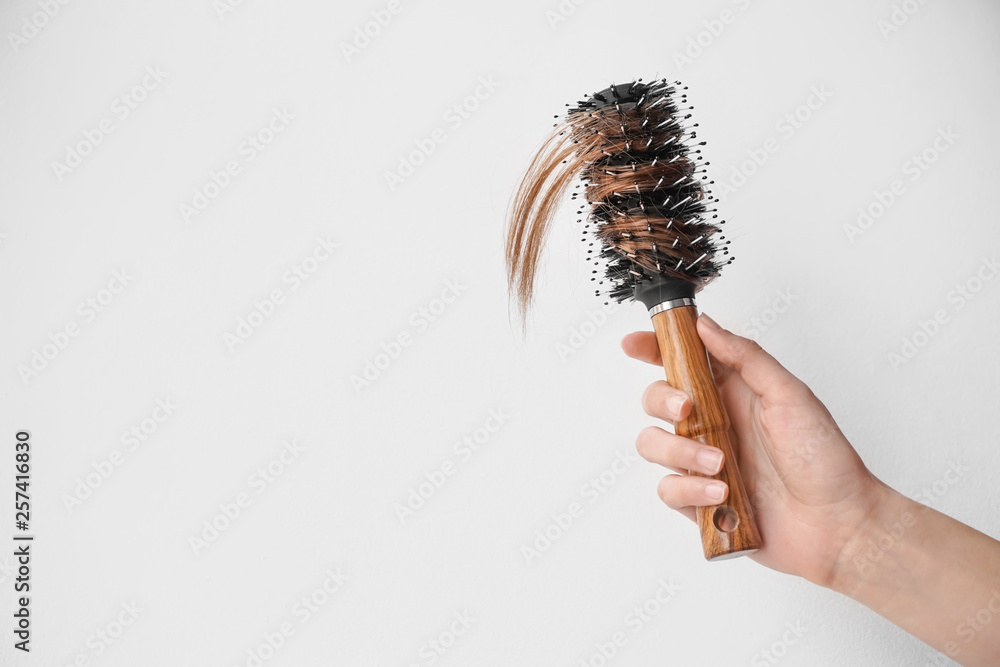 Hand of woman with hair loss problem holding brush on light background