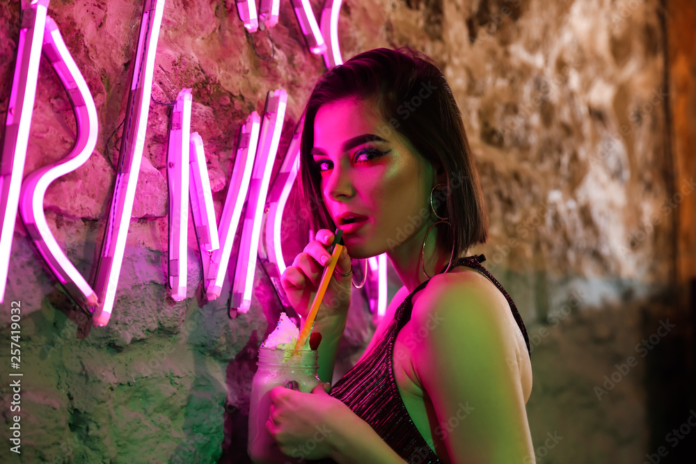 Toned portrait of beautiful young woman near neon lighting on wall