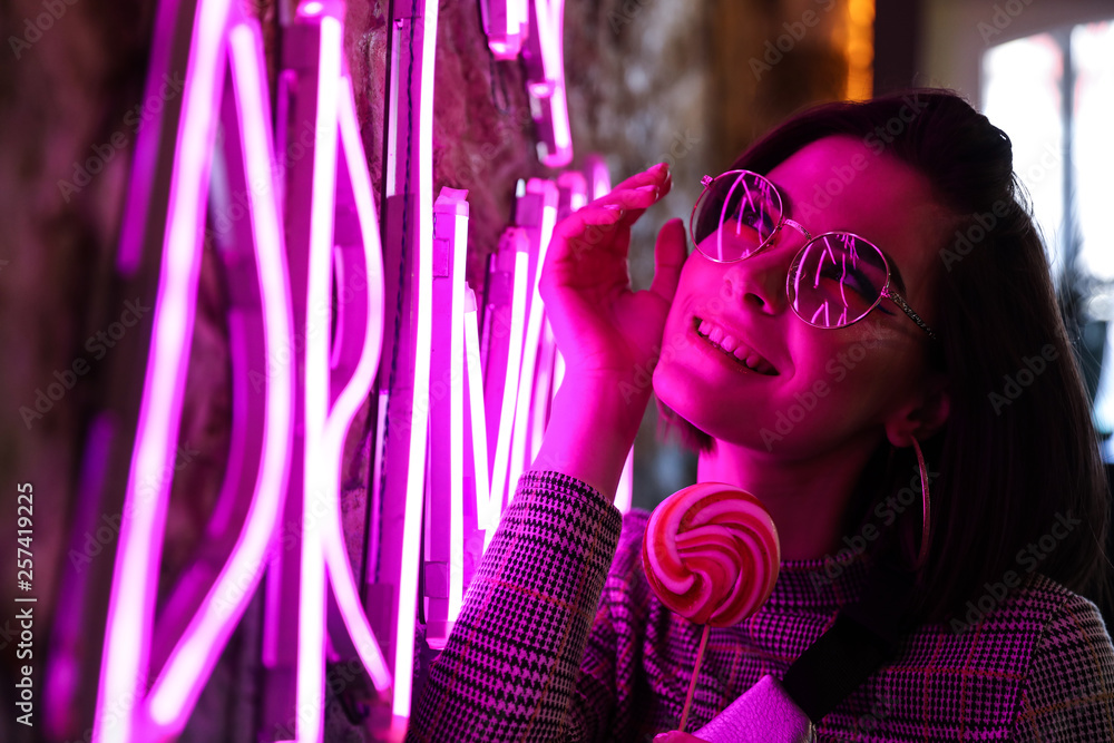 Toned portrait of beautiful young woman near neon lighting on wall