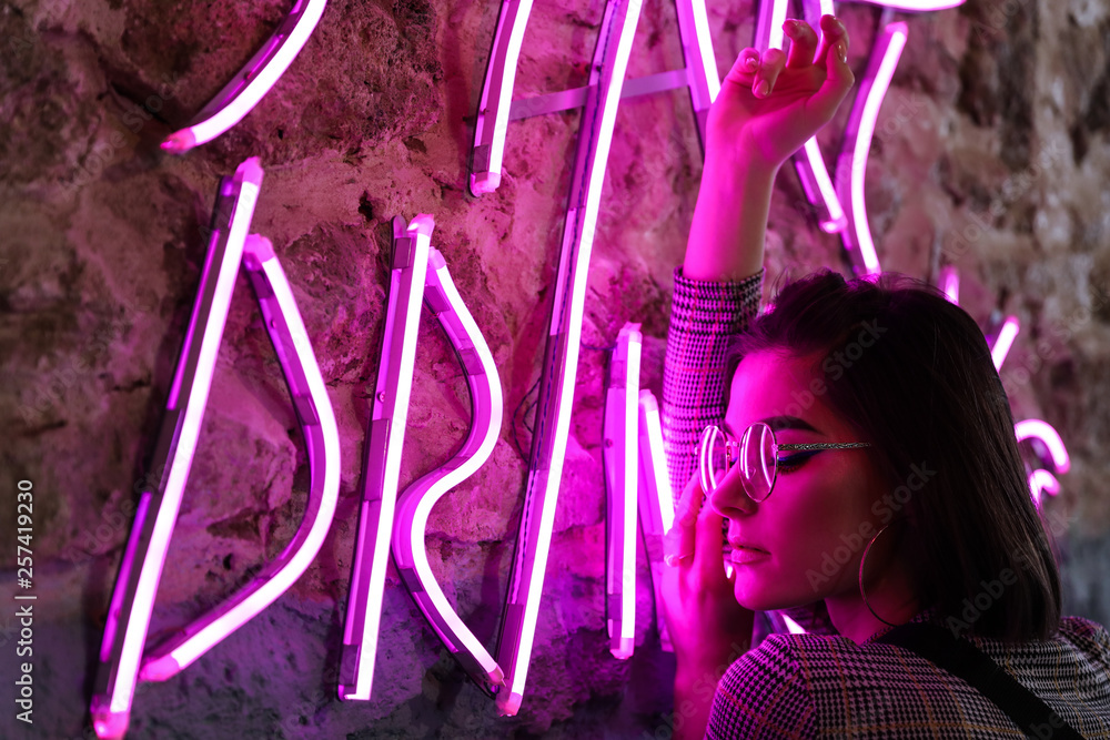 Toned portrait of beautiful young woman near neon lighting on wall