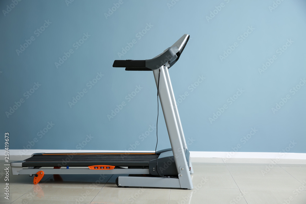 Modern treadmill near color wall in gym