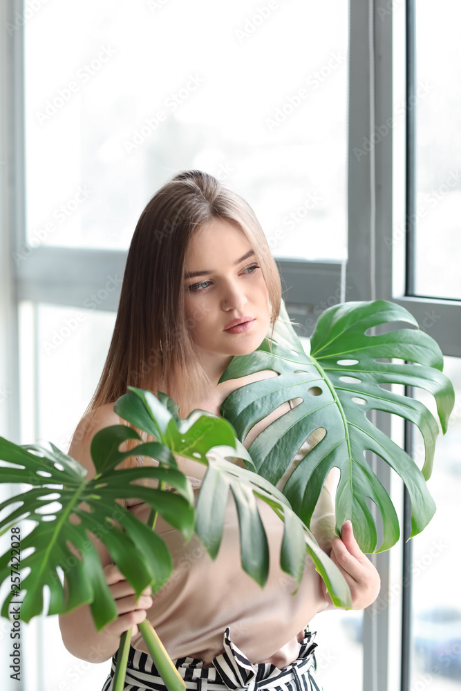 Portrait of beautiful woman with green tropical leaves near window