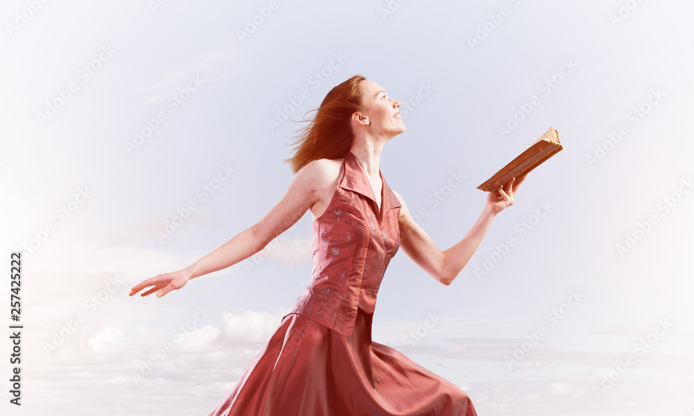 Girl against cloudy sky with opened book in palm as idea for knowledge