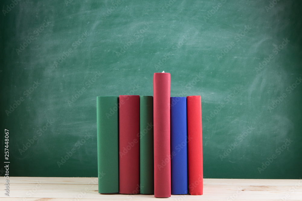 Education and reading concept - group of colorful books on the wooden table in the classroom, blackb