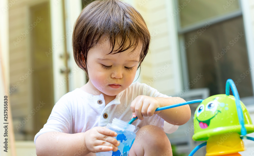 Toddler boy playing with a water sprinkler outside