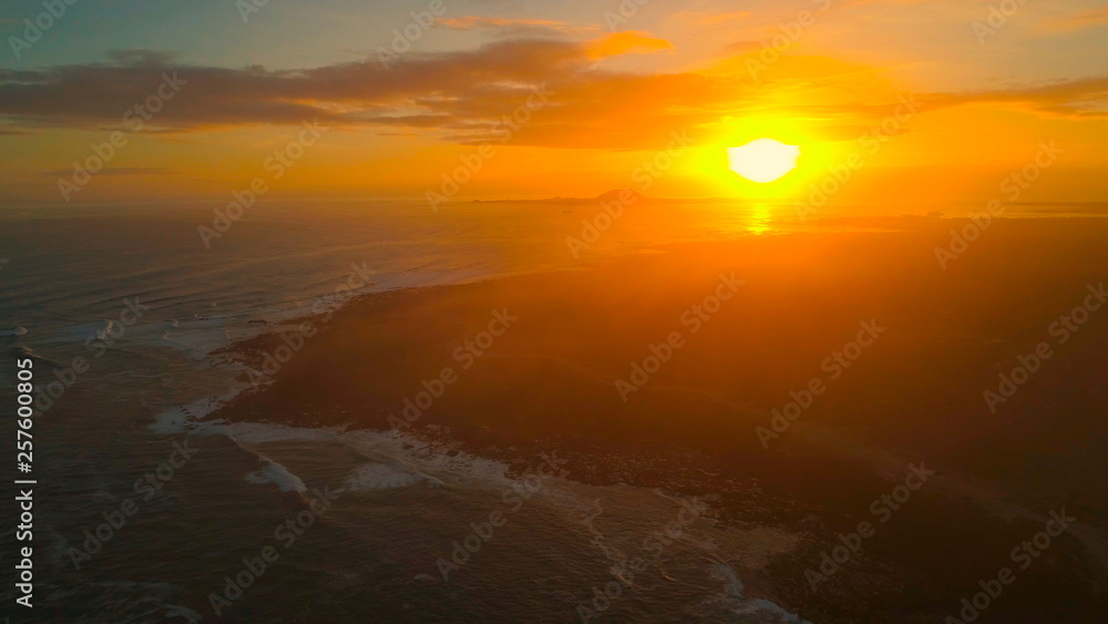 DRONE: Flying above the black rocky shoreline of a remote island at sunrise.