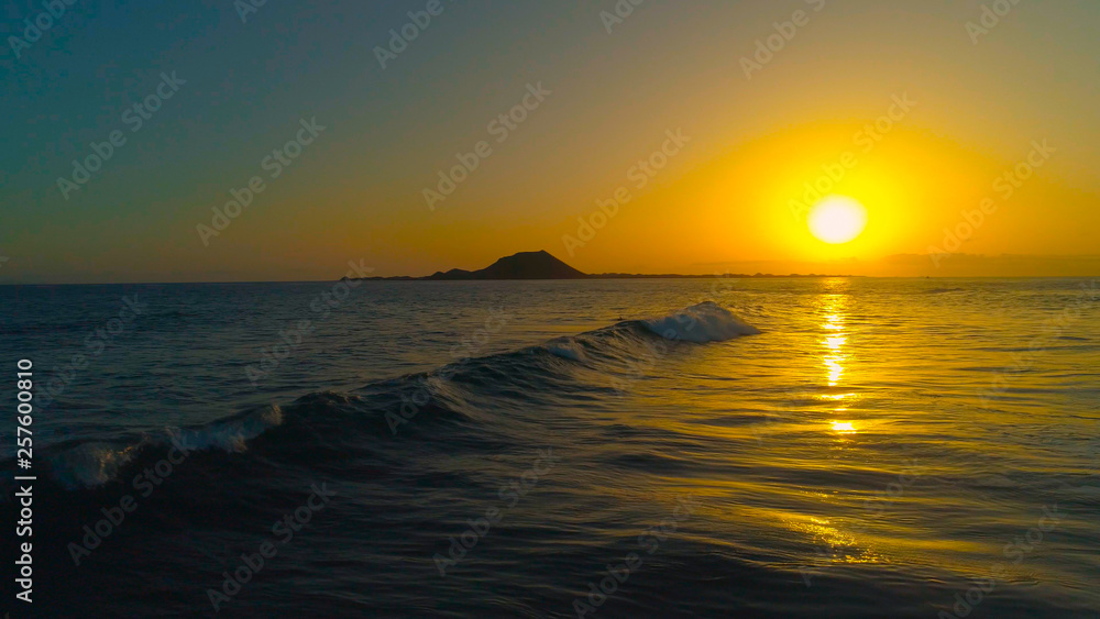 DRONE: Small tube wave rolls towards the beach on a golden summer evening.