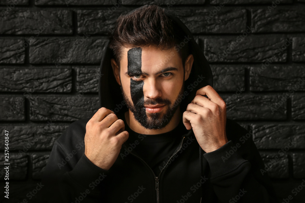 Portrait of handsome man with paint on his face against dark brick background