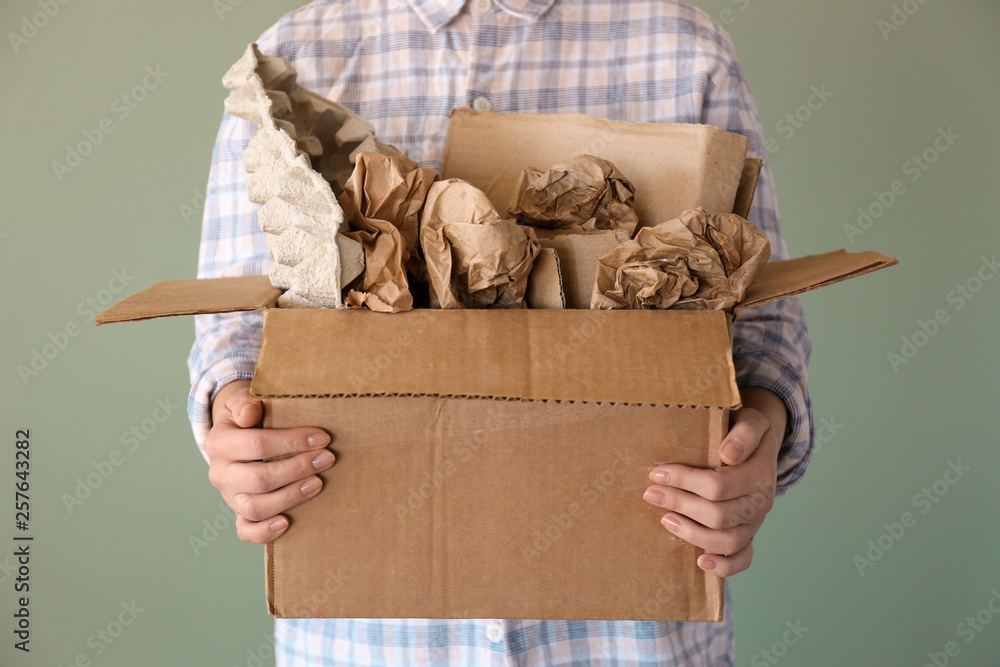 Woman holding box with paper garbage on color background