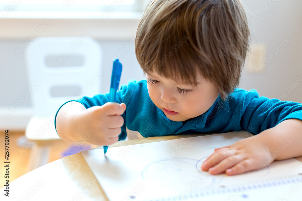 Toddler boy drawing with pen and paper at his desk