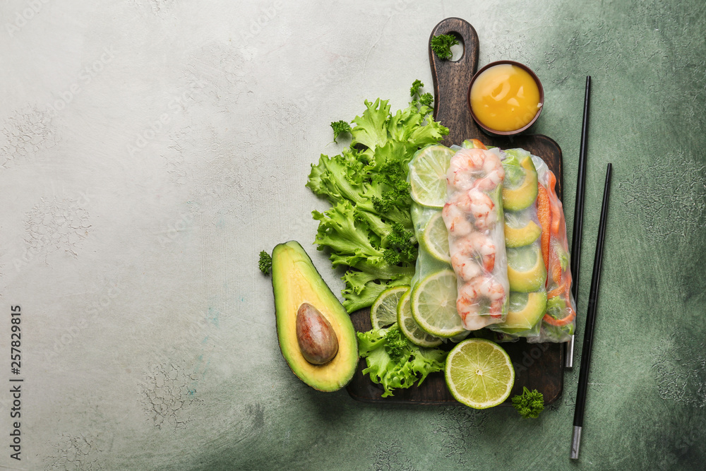 Board with tasty spring rolls on color background