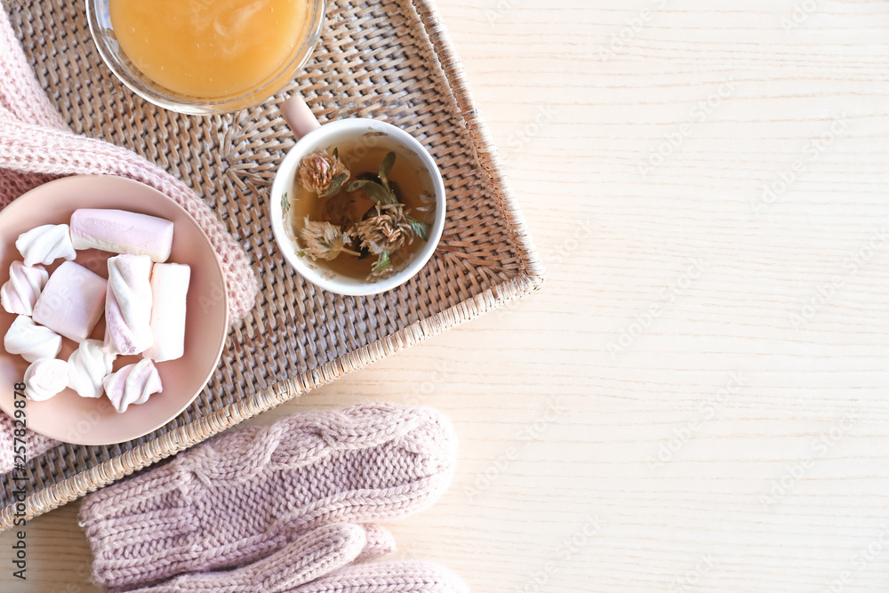 Wicker tray with cup of tea, honey and sweets on table