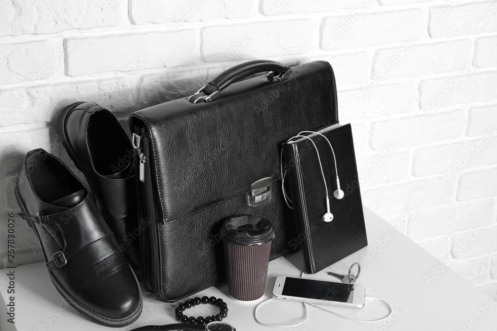 Set of male accessories with mobile phone on table near white brick wall