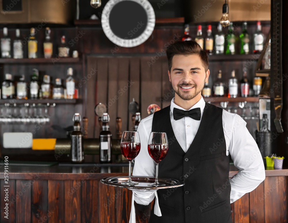 Young male waiter with glasses of wine in restaurant