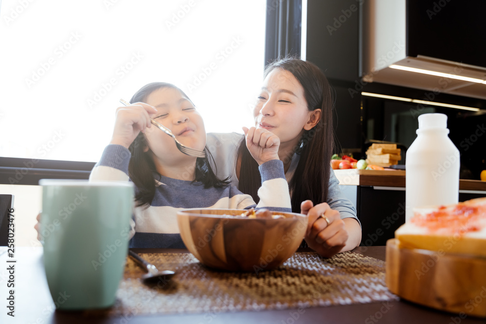 妈妈和女儿在厨房吃牛奶麦片早餐。