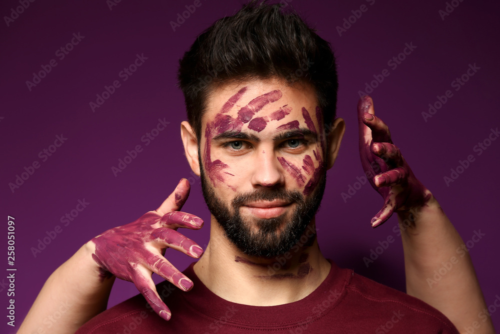 Portrait of handsome man with paint on his face and female hands against color background