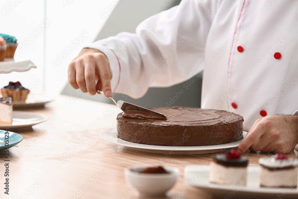 Male confectioner decorating tasty chocolate cake in kitchen, closeup