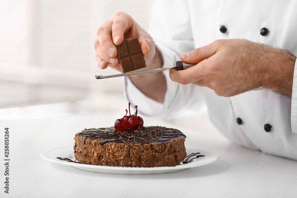 Male confectioner decorating tasty chocolate cake in kitchen, closeup