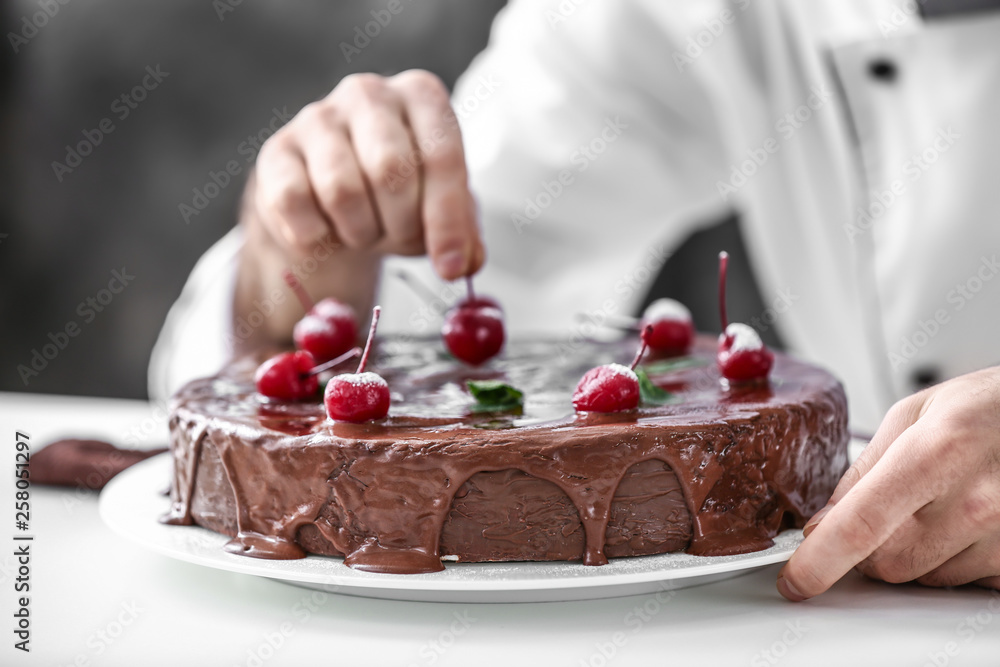 Male confectioner decorating tasty chocolate cake in kitchen, closeup